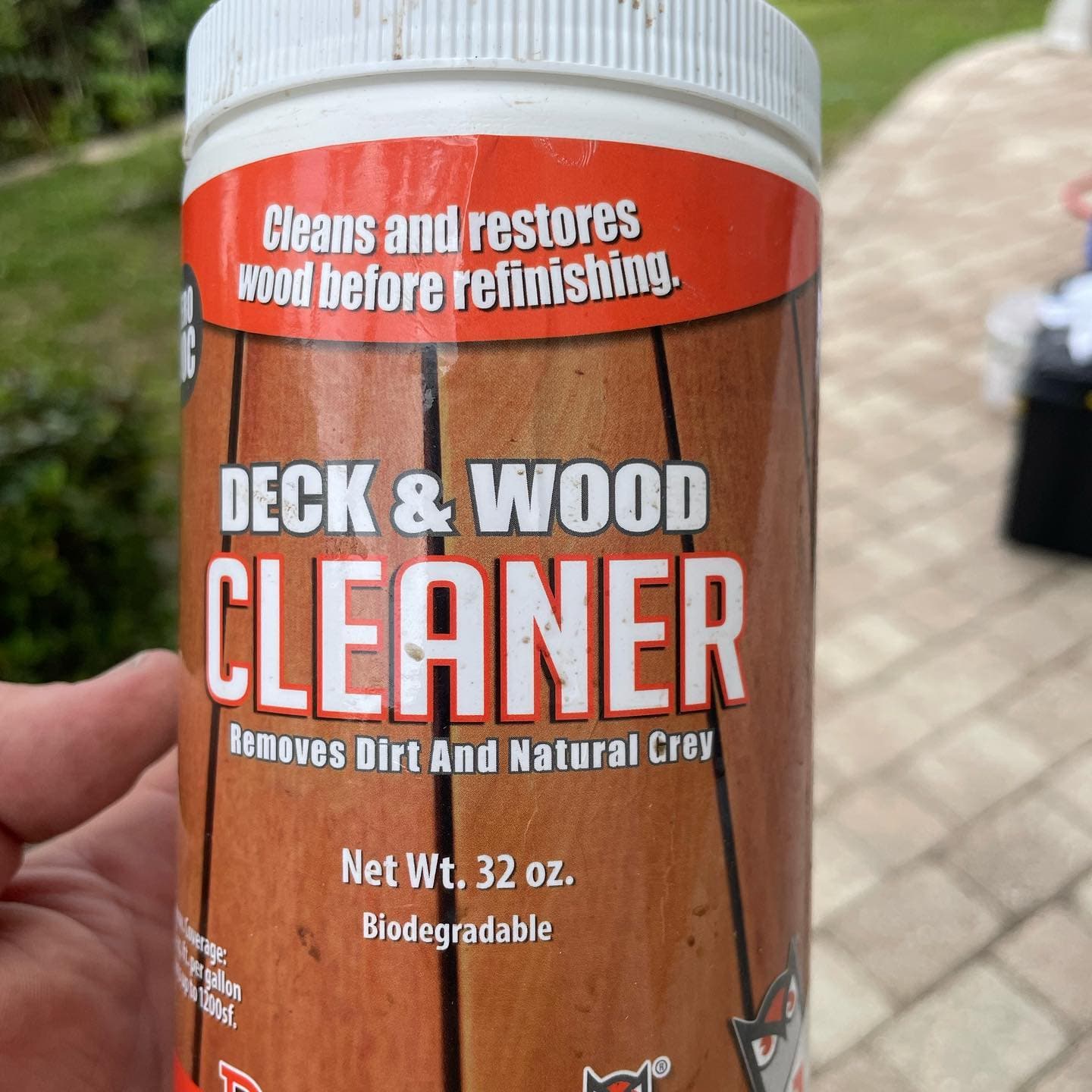 A hand holding a 32-ounce container labeled Deck & Wood Cleaner.