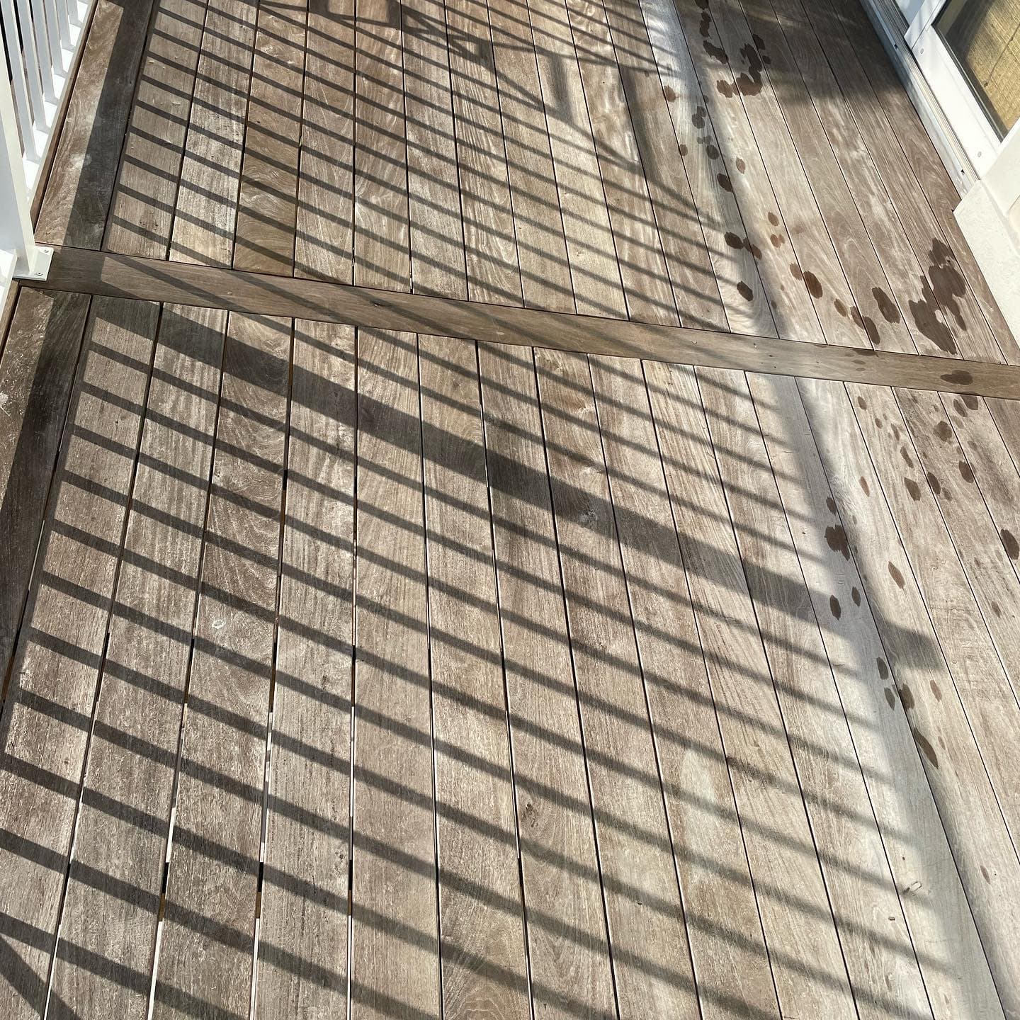 Gray-brown Ipe deck boards with pale weathered areas, dark spots, and shadows from a white railing.