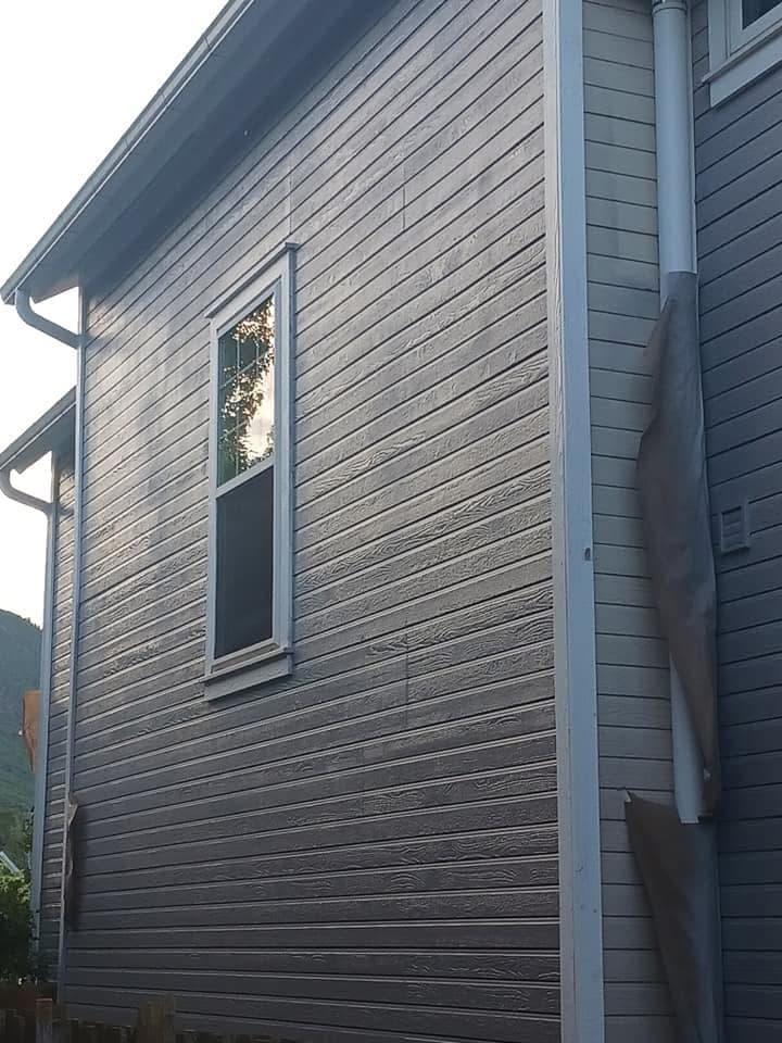Gray horizontal siding around a tall window, with uneven reflective bands visible across the wall.