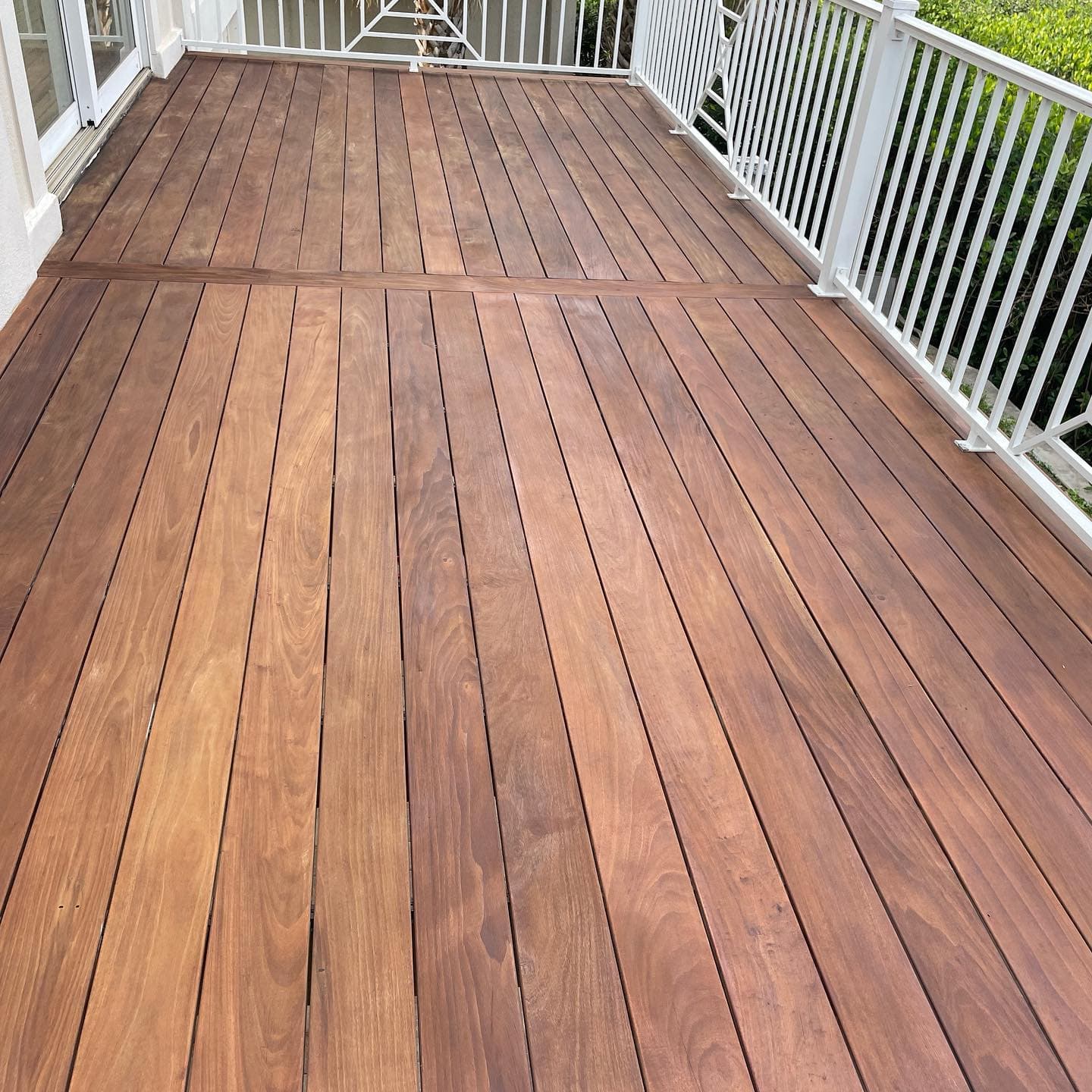 An overview of brown Ipe deck boards with visible grain, bordered by white railings and a sliding door.